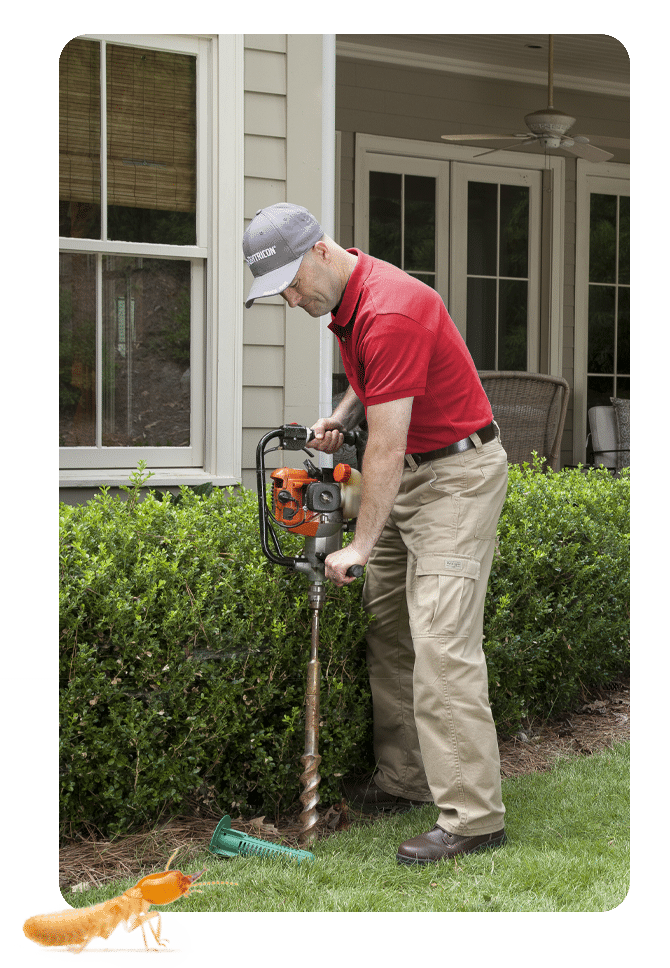 Emtec technician in a red shirt installing a Sentricon termite station beside a house