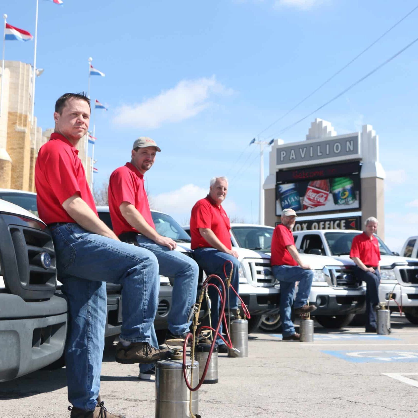 Emtec Pest Control Tulsa Workers in red shirts stand in front of service vehicles