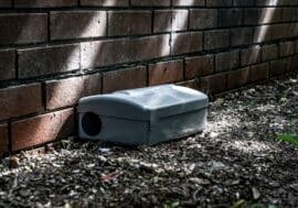Grey Metal external rodent rat bait station outside against a brick wall close up.