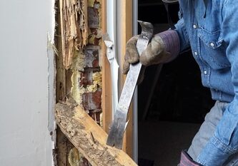 Man prying sheetrock and wood damaged by termite infestation in house.
