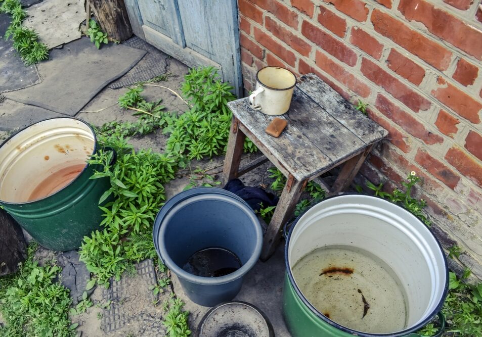 Buckets and large pans of water stand outside near a red brick wall - top view.